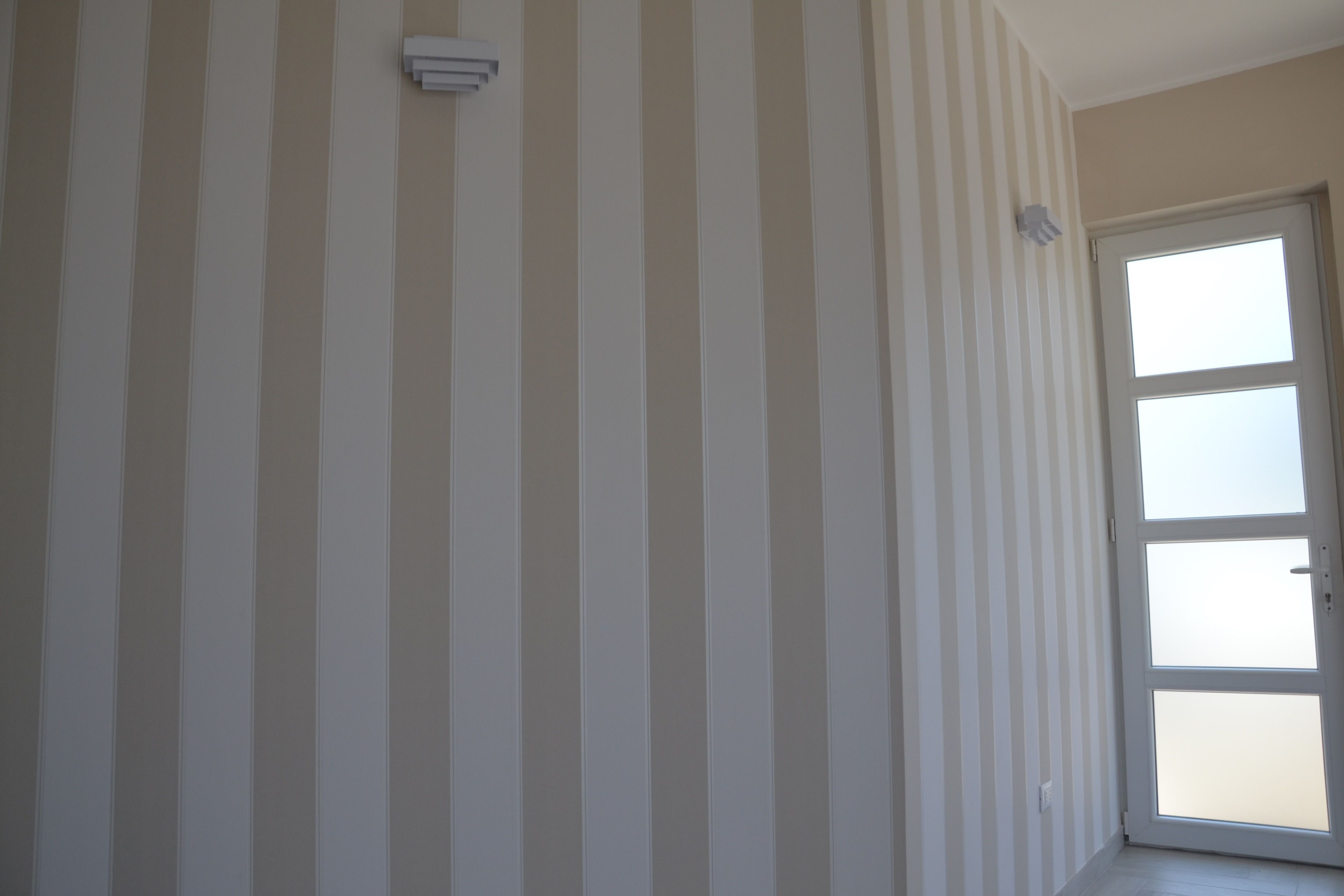 A hallway with striped wallpaper, a door with frosted glass panels, and a smoke detector on the wall.
