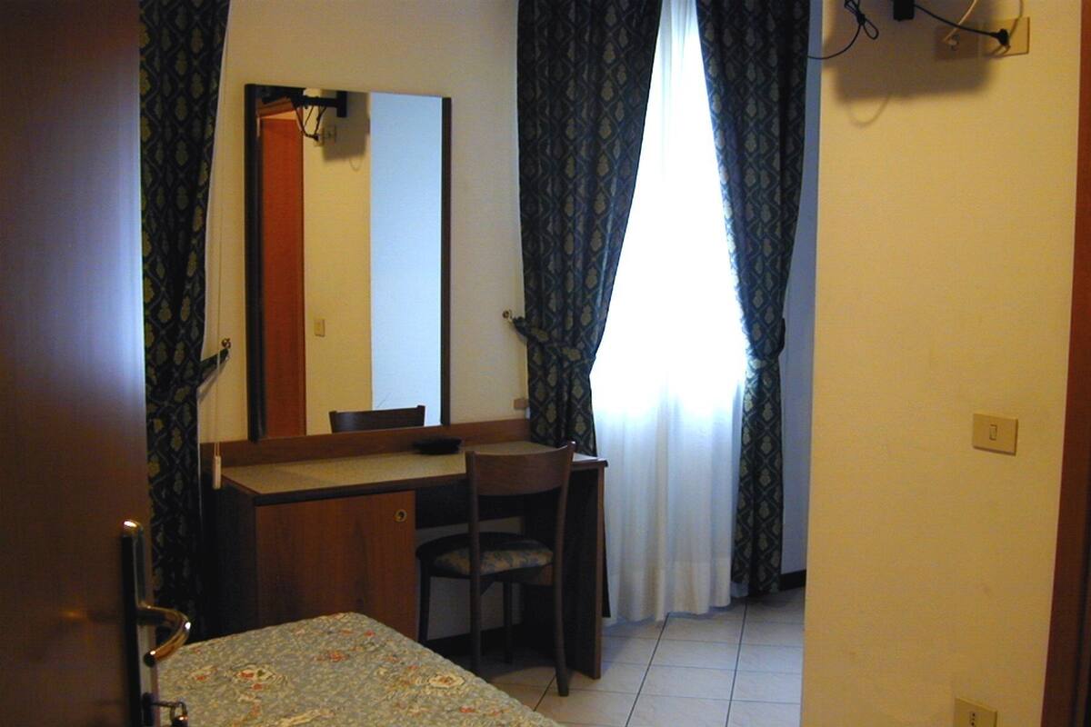A small, simple room with a bed, a desk, a chair, and a mirror.