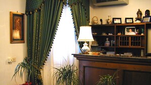 A room with a wooden desk, a lamp, a bookshelf, and a window with curtains. - Hotel Astoria (Viareggio)