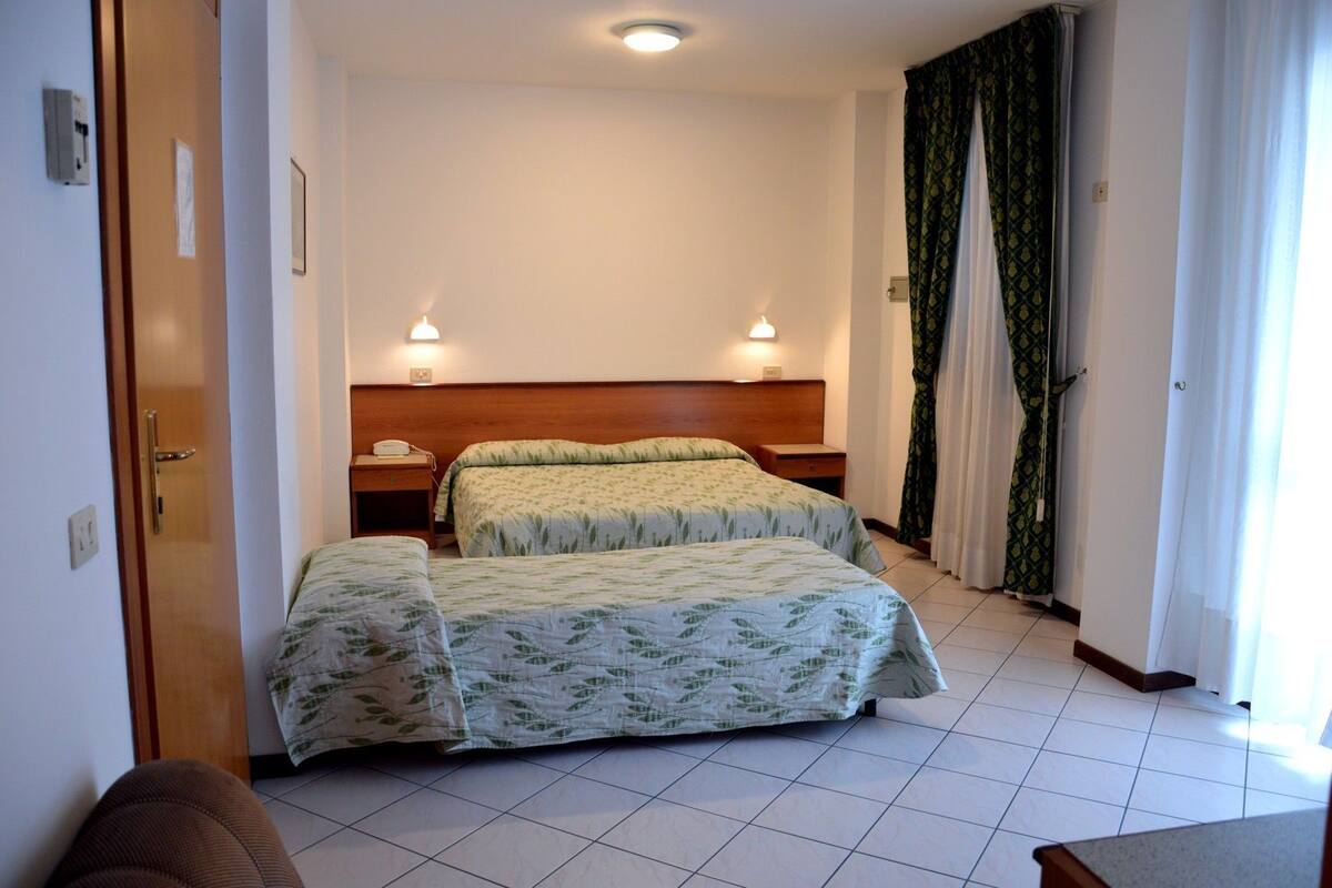 A hotel room with two beds, a wooden headboard, bedside lamps, a telephone, and a door.