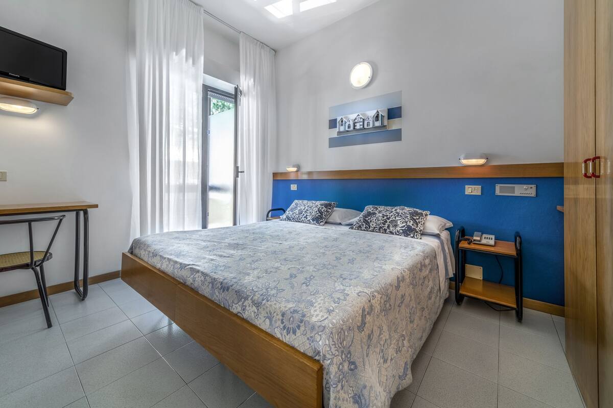 A bedroom with a bed, bedside tables, a desk, and a television.