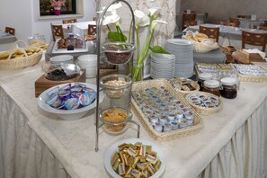 A buffet table with various food items and containers, including fruits, breads, and condiments. - Hotel Morotti (Misano Adriatico)