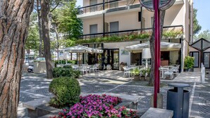 A multi-story building with outdoor seating and a tree in the foreground. - Hotel Morotti (Misano Adriatico)
