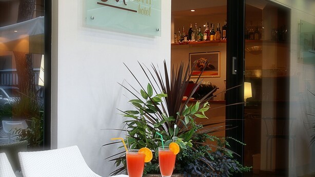 A modern hotel lobby with a white reception desk, a glass wall with a sign reading "Morotti Hotel", and a bar area visible through the doorway. - Hotel Morotti (Misano Adriatico)