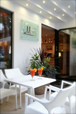 A modern hotel lobby with a white reception desk, a glass wall with a sign reading "Morotti Hotel", and a bar area visible through the doorway. - Hotel Morotti (Misano Adriatico)