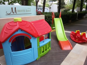 Zona de juegos infantiles con un tobogán y una casita.