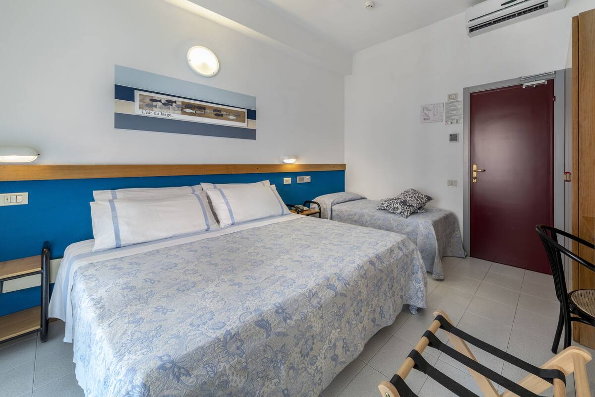 A hotel room with two beds, a wooden headboard, a framed picture on the wall, a door with a handle, and a chair.