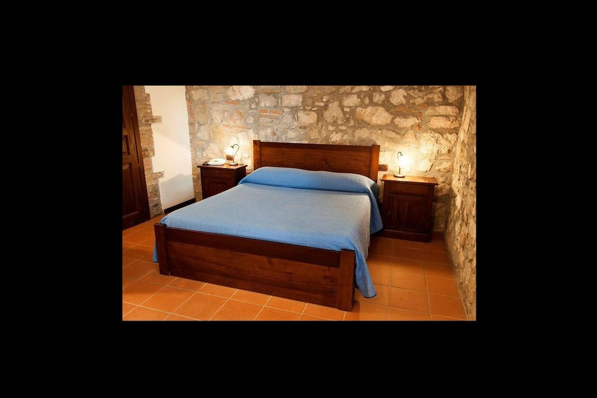 A bedroom with a stone wall, a wooden bed, and two bedside tables with lamps.