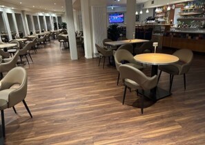 A spacious indoor area with multiple seating arrangements, including round tables and chairs, and a bar area visible in the background. - Highway Hotel (Herbolzheim)
