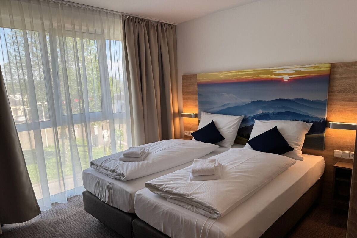 A double bed with white linens, two pillows, and a headboard with a painting of a sunset.