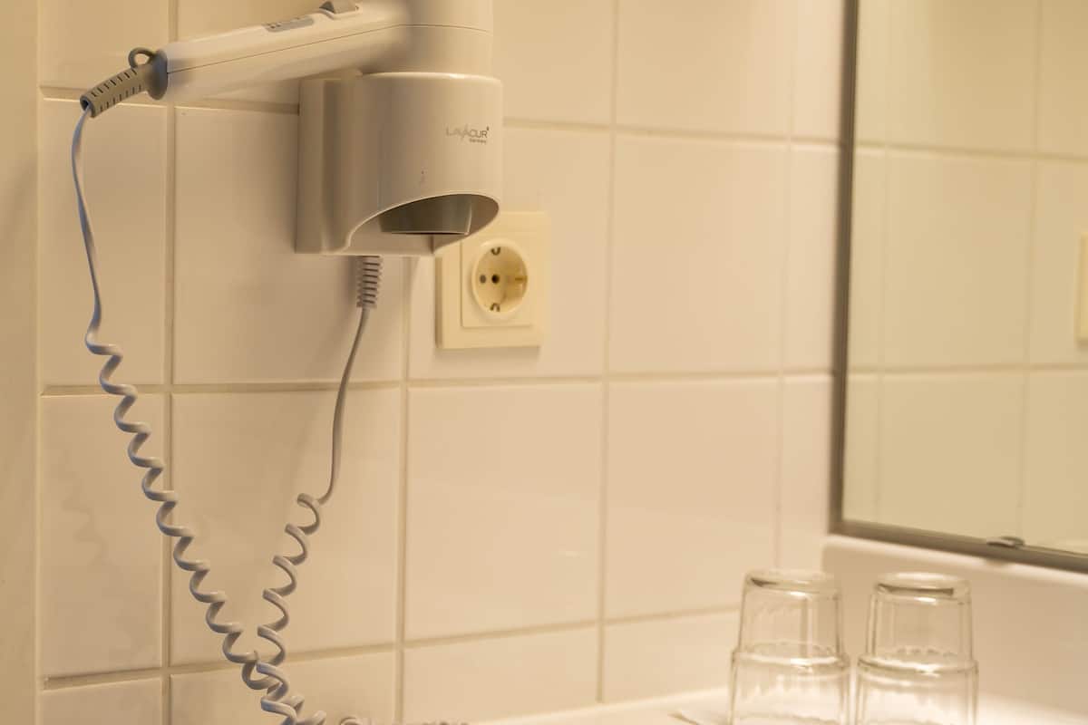 A bathroom with a white sink, a hairdryer, and two clear glasses on the counter.