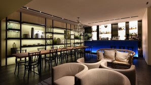 Zona de bar moderna con una mesa de madera larga, asientos acolchados y estanterías con cristalería.