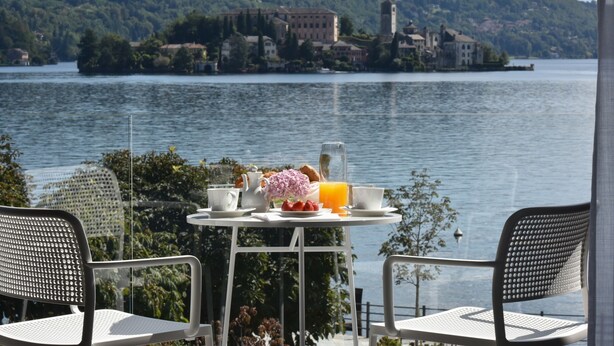 Una mesa con alimentos para el desayuno y dos sillas mirando a un lago con edificios al fondo.