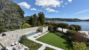 Un jardín ajardinado con piscina, mobiliario exterior y vista a un lago.
