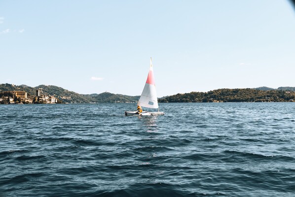 A sailboat on a calm body of water with a hilly landscape in the background. - Hotel Casa Fantini (Pella)