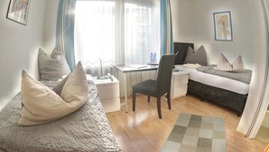 Una habitación de hotel compacta con una cama, un escritorio, una silla y una computadora.