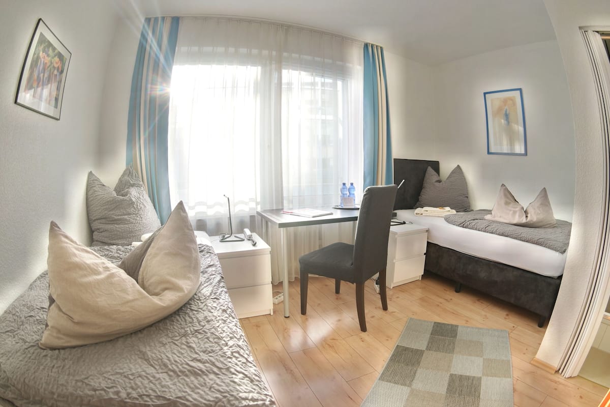 Una habitación de hotel compacta con una cama, un escritorio, una silla y una computadora.