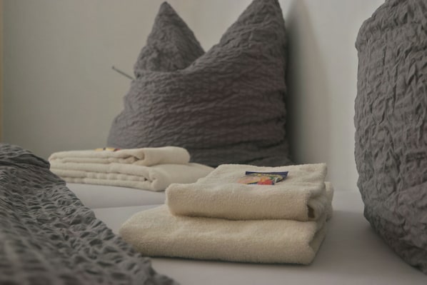 Una cama bien hecha con toallas dobladas y dos almohadas grises.