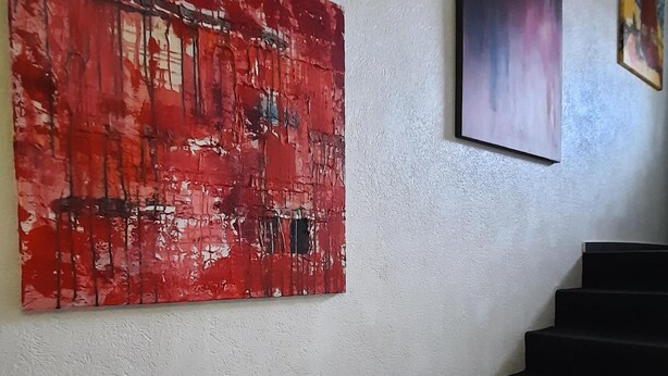 Una escalera con barandilla que lleva a un rellano donde tres obras de arte están exhibidas en la pared.