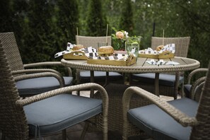Mesa de jantar redonda ao ar livre com cadeiras de vime, toalha xadrez e um arranjo floral.