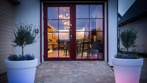 A building entrance with double glass doors, a brick pathway, and two large potted plants. - Domki  Polanki 23 (Wicko)