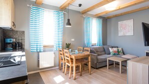A modern kitchen with a black countertop and a coffee machine, a dining area with a wooden table and chairs, and a living area with a sofa and a TV. - Domki  Polanki 23 (Wicko)