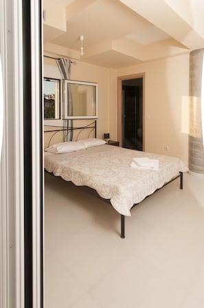 A bedroom with a bed, a TV, and a bathroom visible through an open door. - Elia & Thalassa (Kalamata)