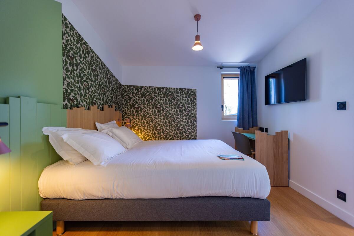 Een moderne slaapkamer met een groot bed, een flatscreen televisie en een bureau met een stoel.