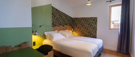 Un dormitorio con cama, un escritorio y una silla. Hay una ventana con cortinas.