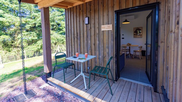Een houten terras met een tafel en stoelen, een bordje met een kamer nummer, en uitzicht op de omgeving.