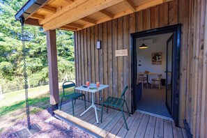 Um deck de madeira com uma mesa e cadeiras, uma placa indicando um número de quarto e vista para o exterior.