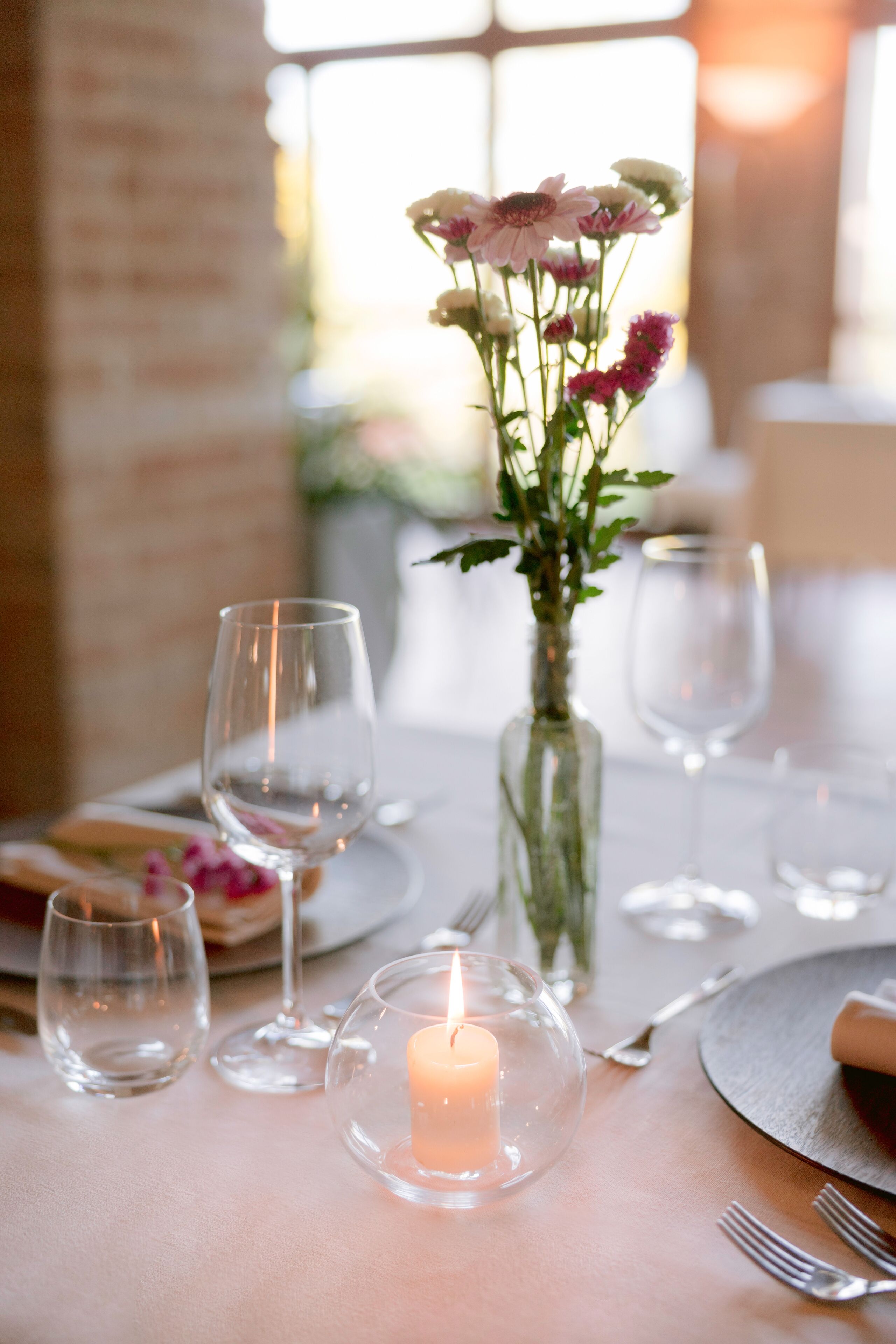 Une table dressée pour le dîner, avec une bougie, un vase rempli de fleurs et des verres à vin vides.