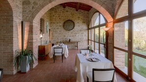 A dining area with brick walls, large windows, and a rustic stone ceiling. Tables are set with white tablecloths and candles. - Borgo Sant'Ambrogio Resort (Trequanda)