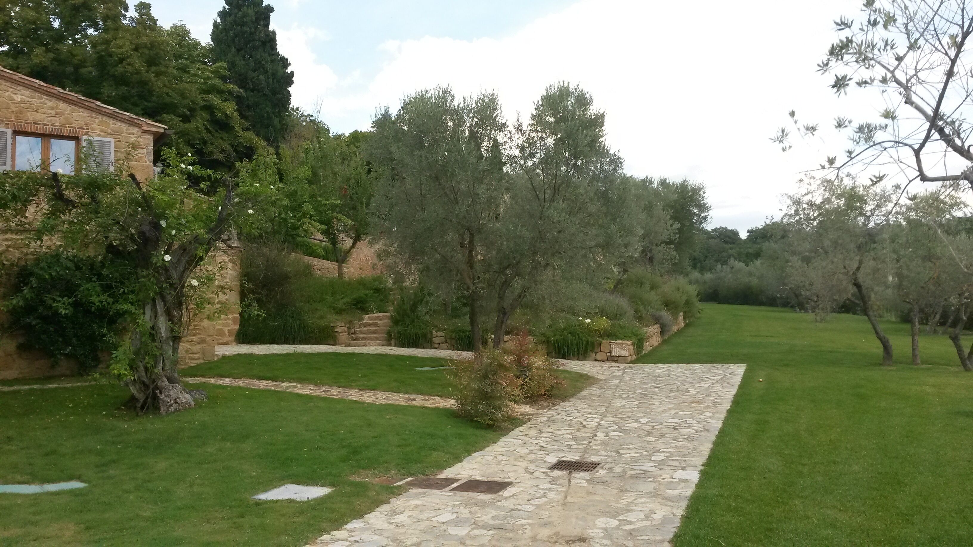A stone pathway leading through a well-maintained garden with a stone building on the left.