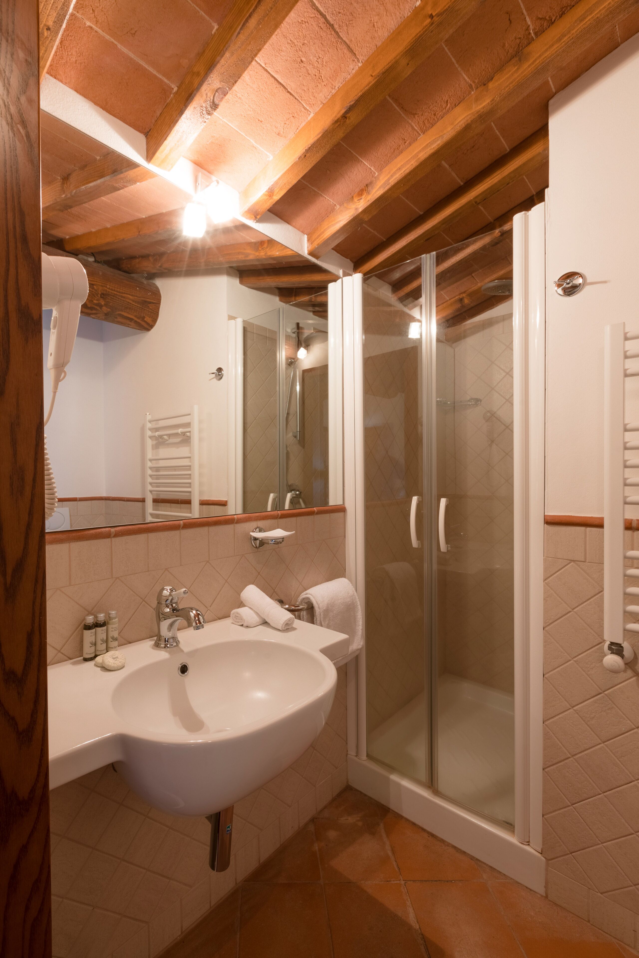 A bathroom with a white sink, a glass-enclosed shower, and wooden beams on the ceiling.