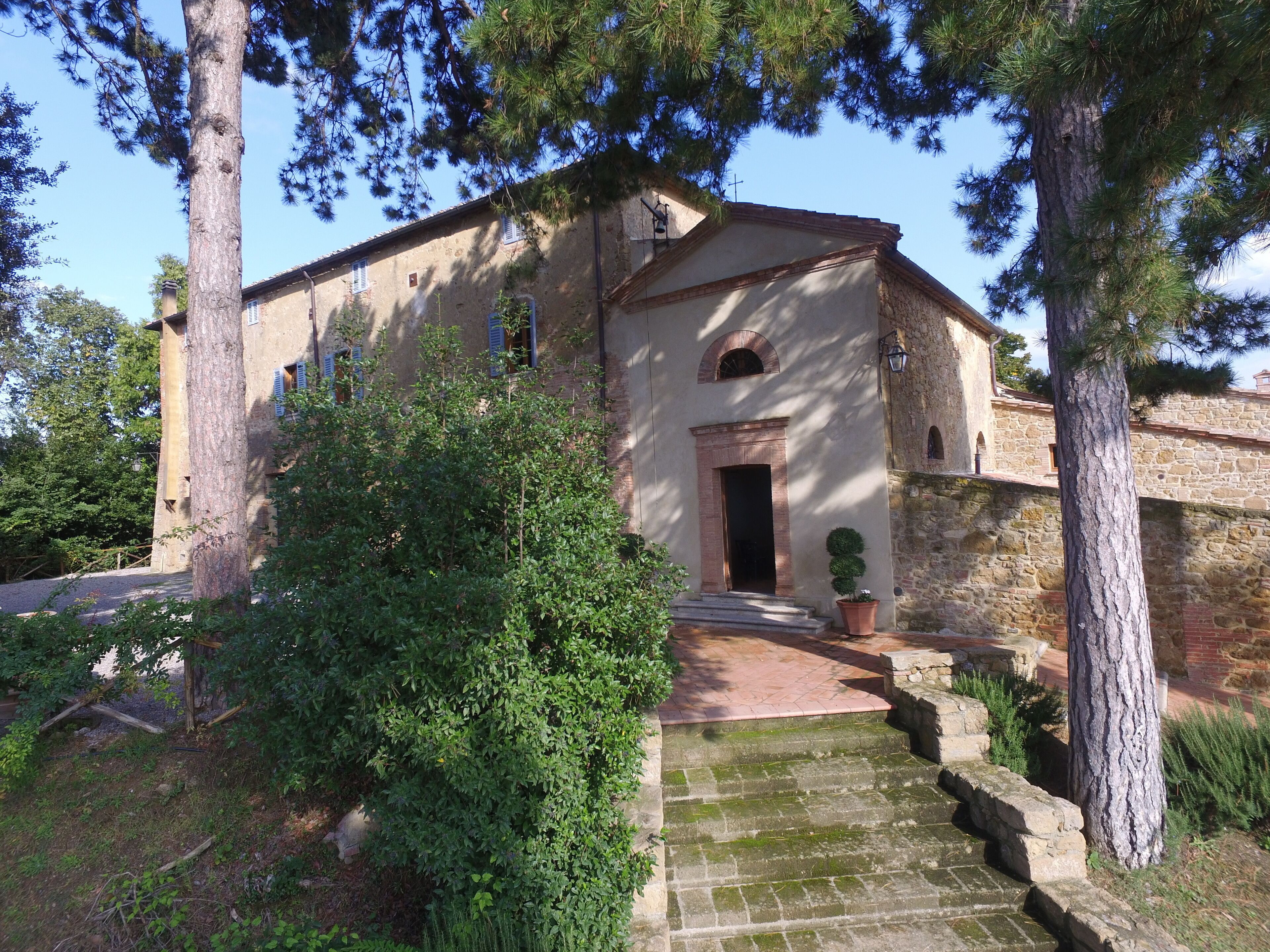 Un edificio de piedra con una entrada central, rodeado de árboles y un pequeño jardín.