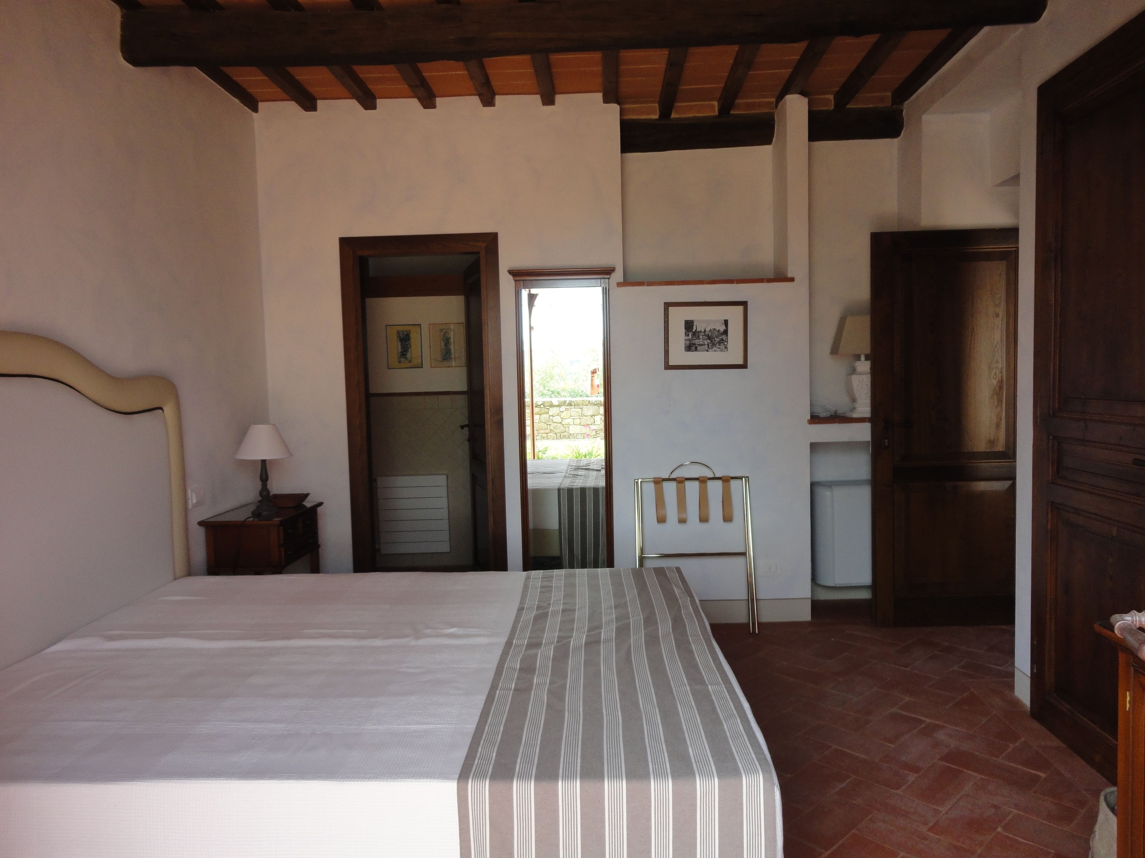 A bedroom with a bed, a nightstand, a chair, a door, and a small table with a lamp.