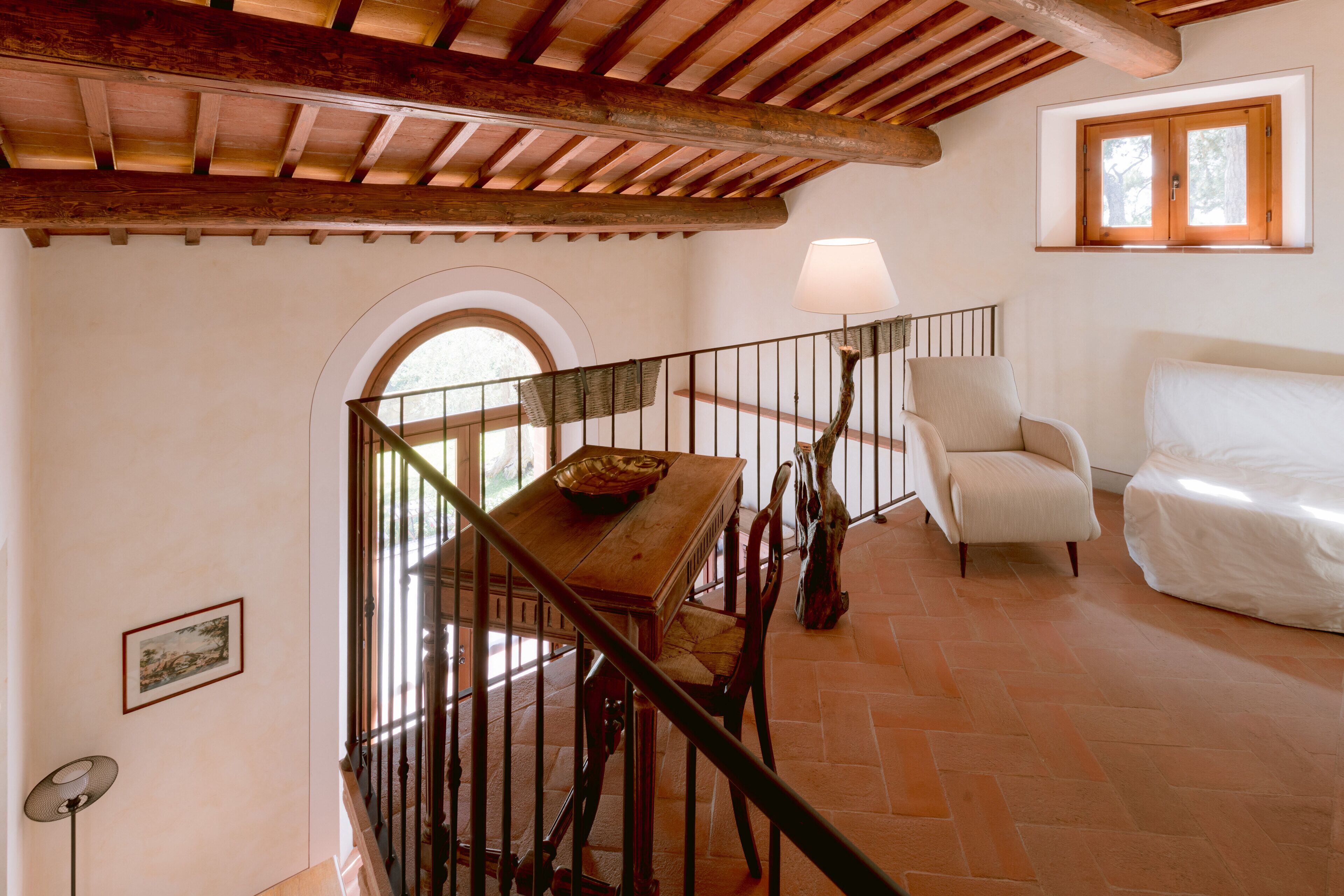 A spacious room with a wooden staircase, a dining table with chairs, a white sofa, and a lamp.