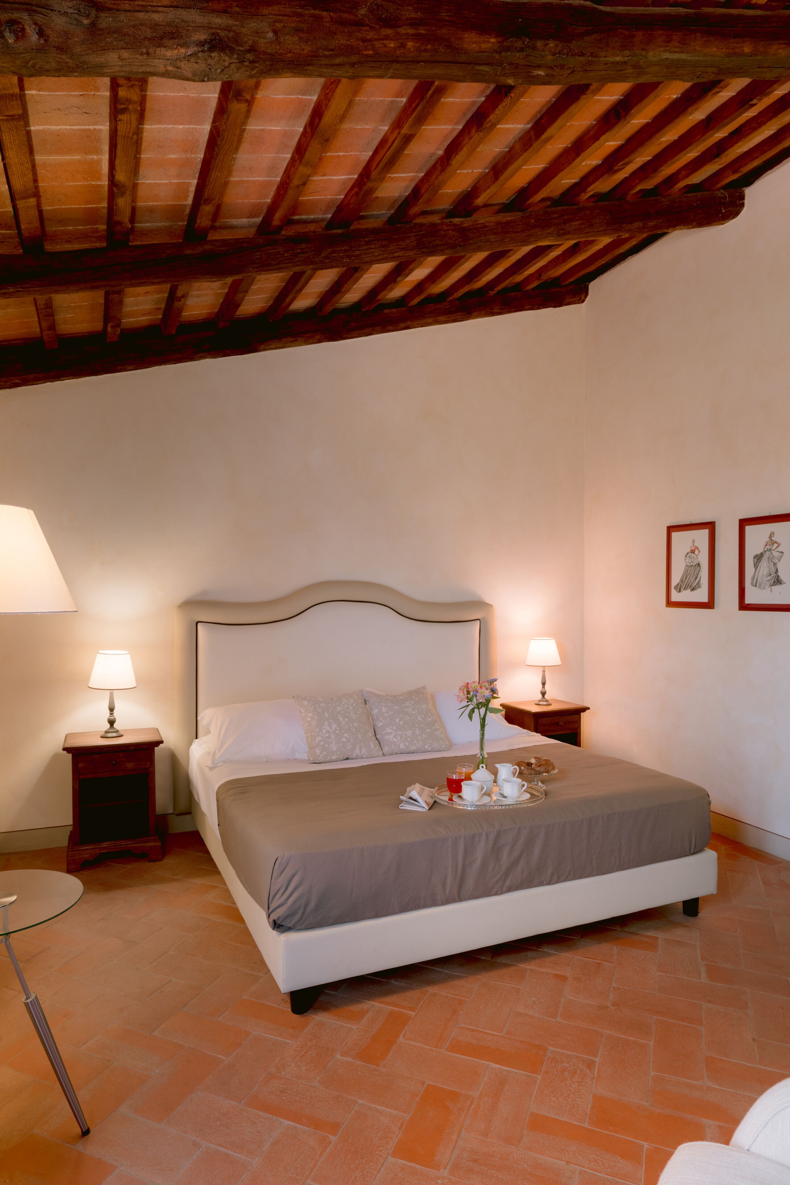 A bedroom with a bed, two bedside tables, a lamp, a tray with items, and a framed picture on the wall.