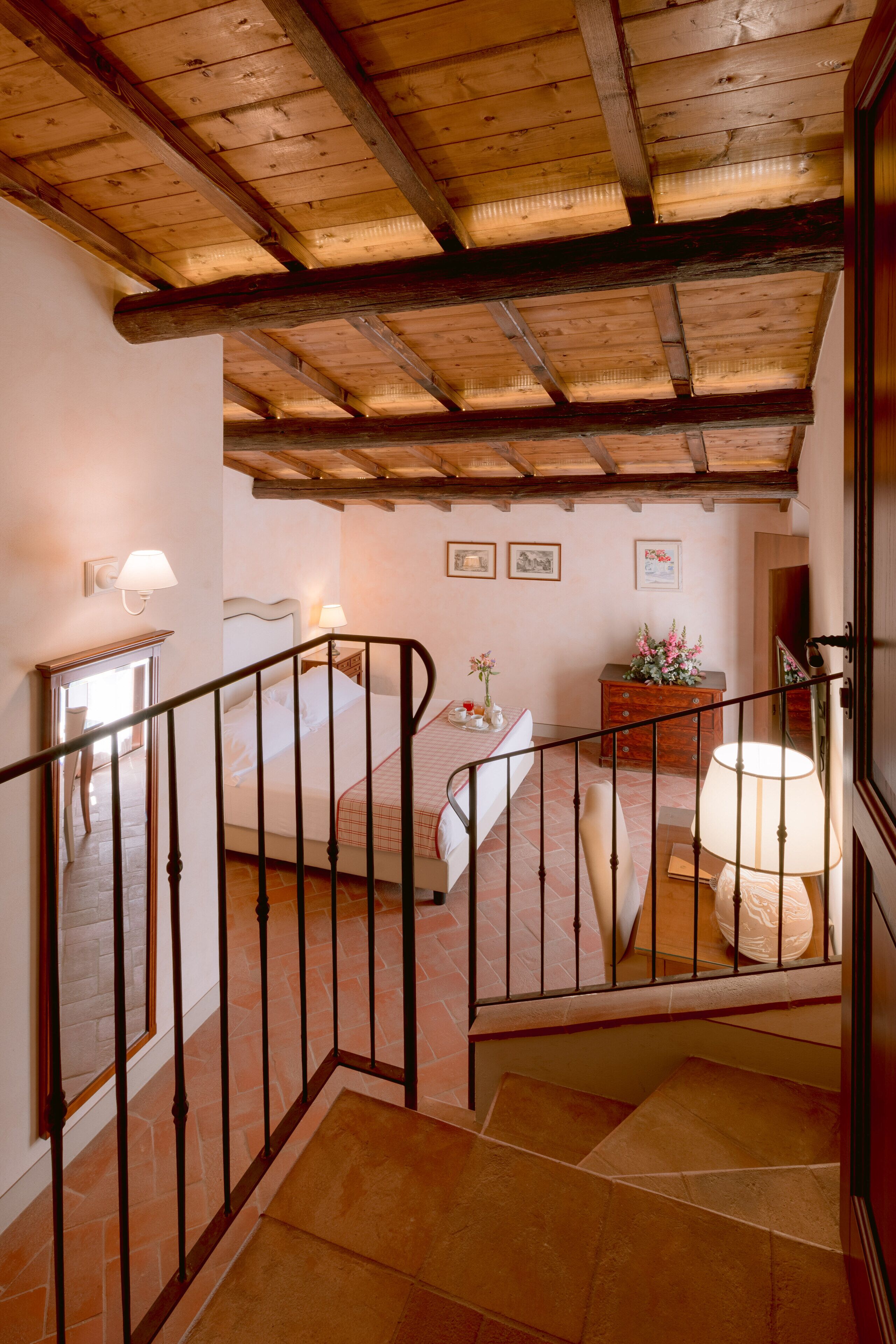 Eine Treppe mit Holzboden und Blick auf ein Schlafzimmer mit Bett, Schminktisch und Wandleuchten.
