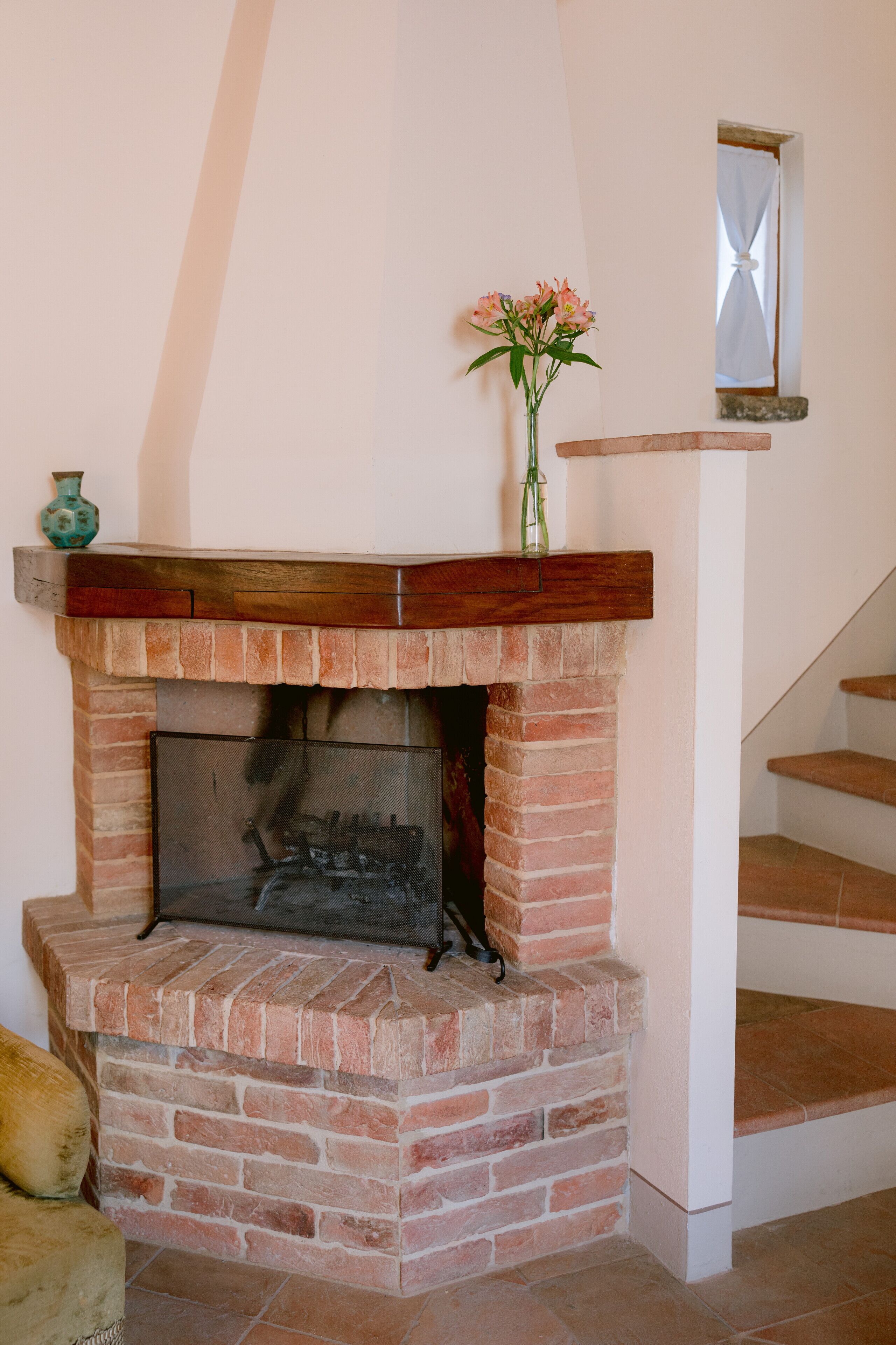 Una chimenea de ladrillo con un alero de madera, un florero con flores y una ventana pequeña encima.
