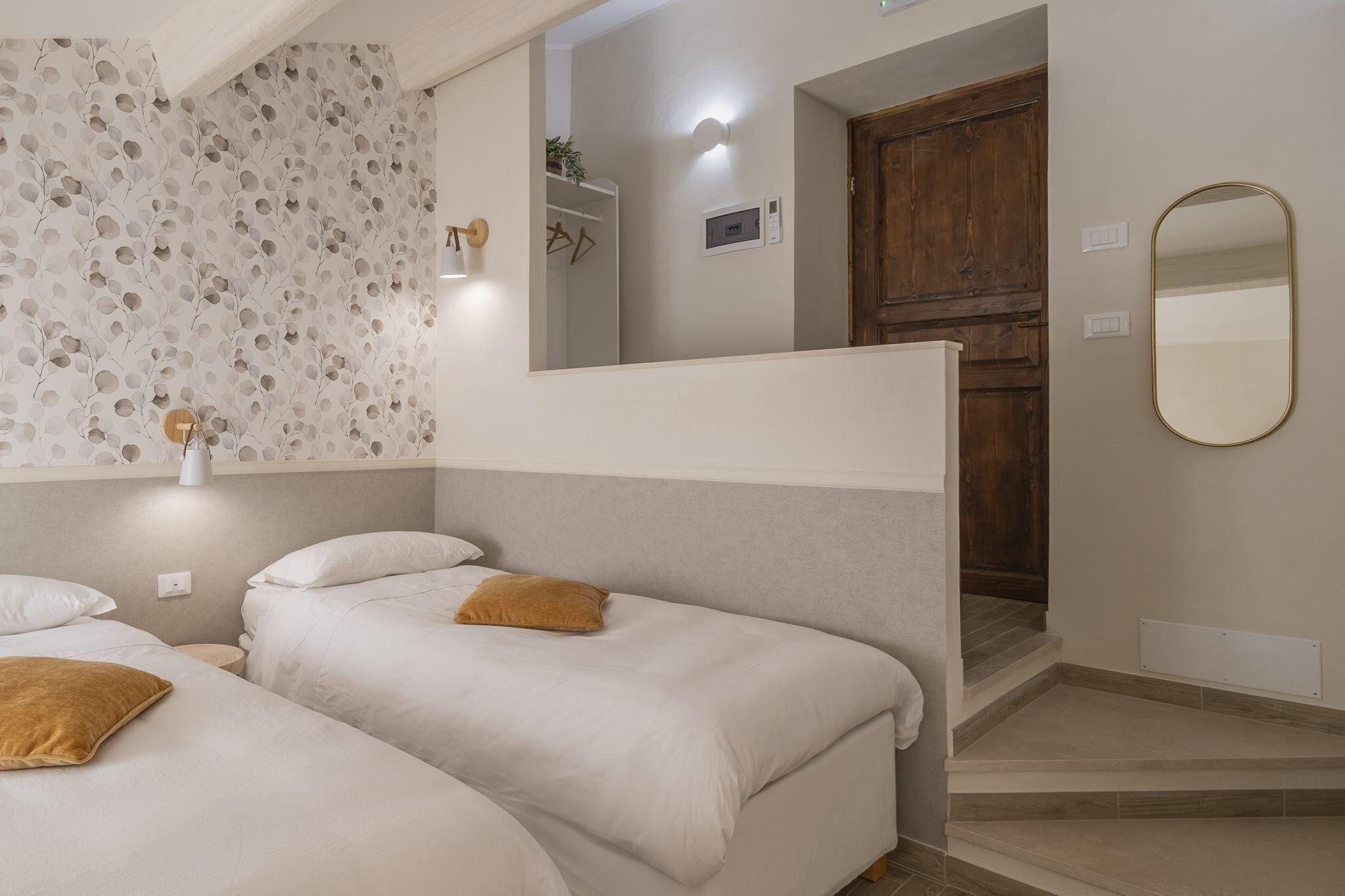 Une chambre avec deux lits, une porte en bois, un miroir et un luminaire fixé au mur.