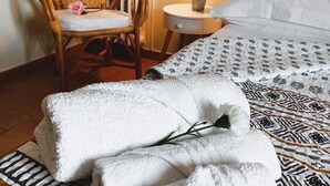 A neatly made bed with patterned bedding, a white fluffy towel, a wicker chair with a cushion, and a small potted plant on a bedside table. - B&B La Rocca (Caprarola)