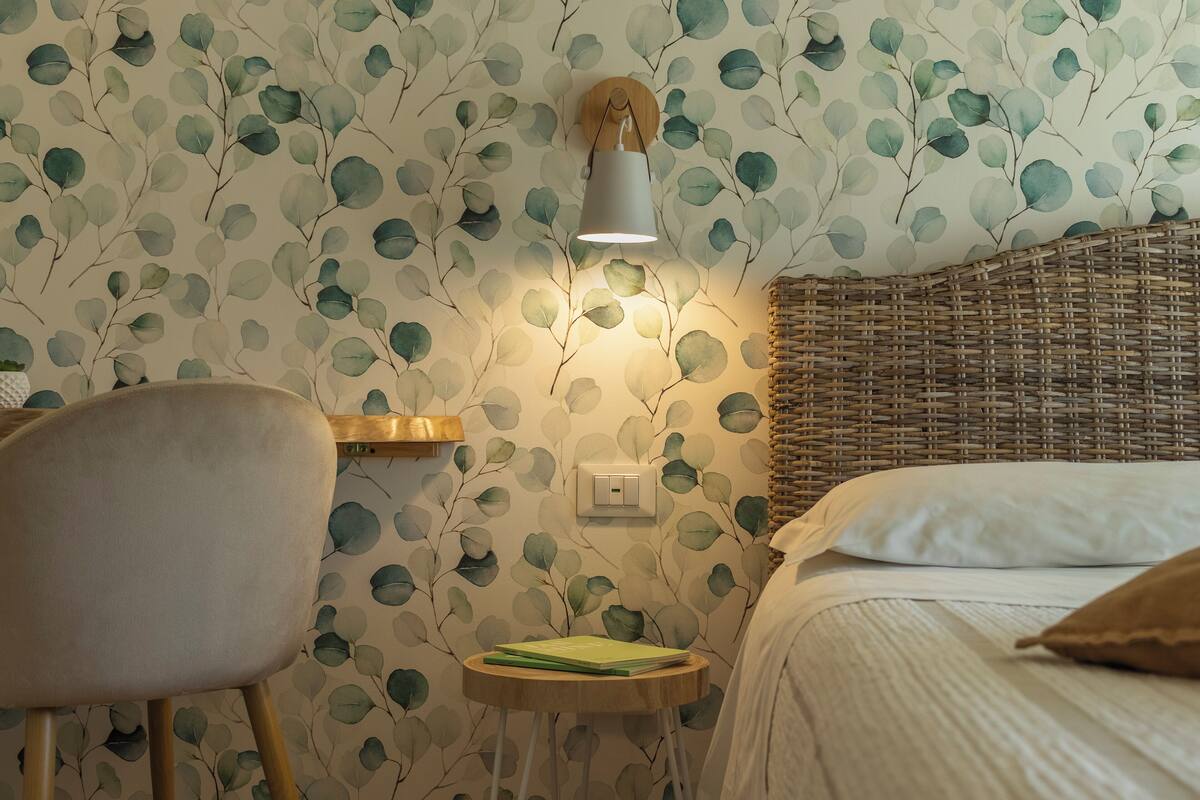 A room with a bed, a chair, a small table, and a wall-mounted lamp.