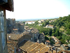A view of a town with terracotta-roofed buildings, a mix of old and new architecture, and a hilly landscape in the background.