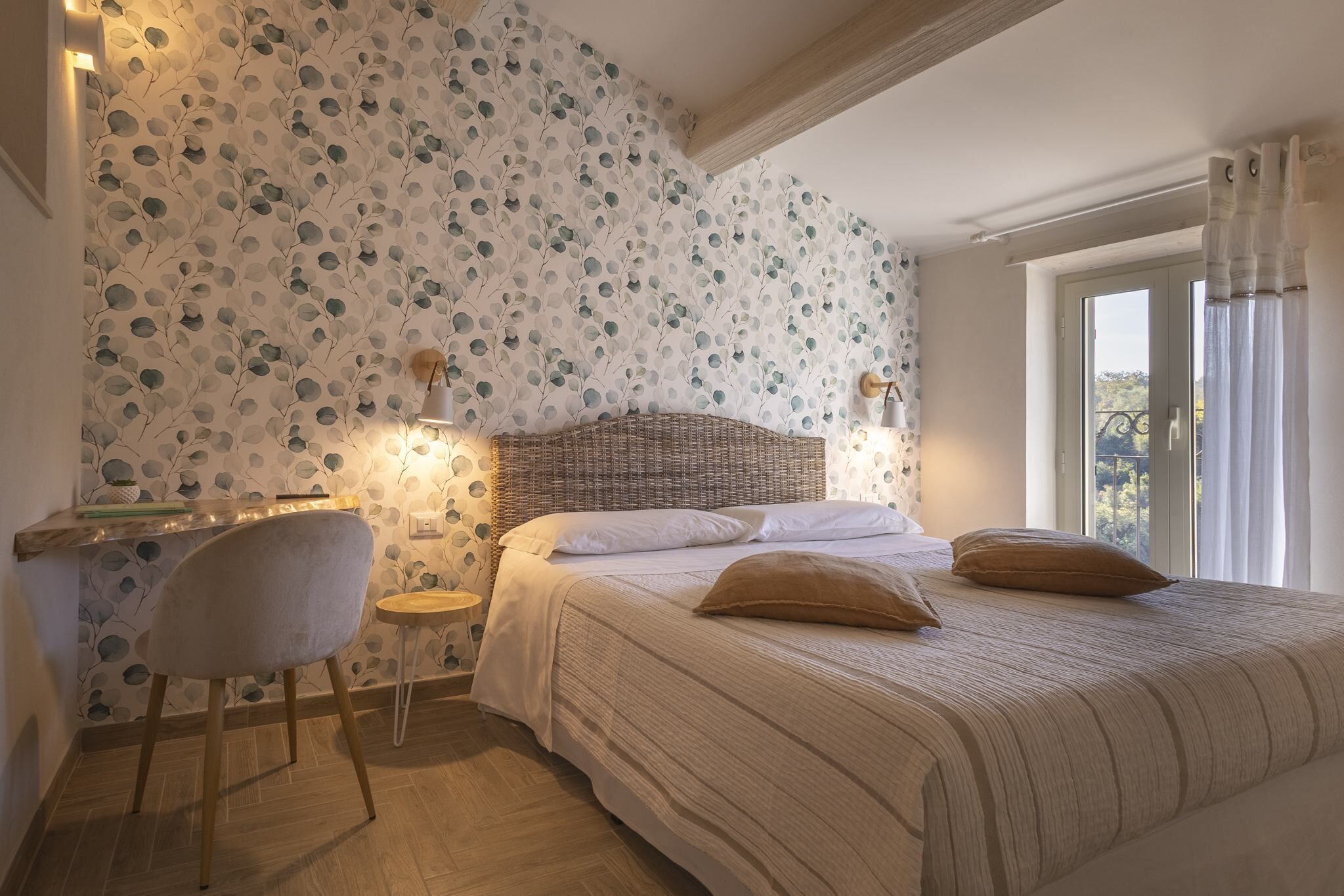Ein Schlafzimmer mit einem Bett, einem Sessel, einem kleinen Tisch und einem Fenster mit Vorhängen.