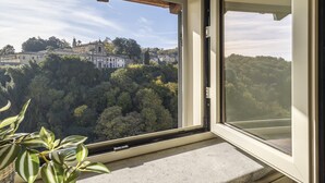 A room with a large window overlooking a forested area and a historic building. - B&B La Rocca (Caprarola)