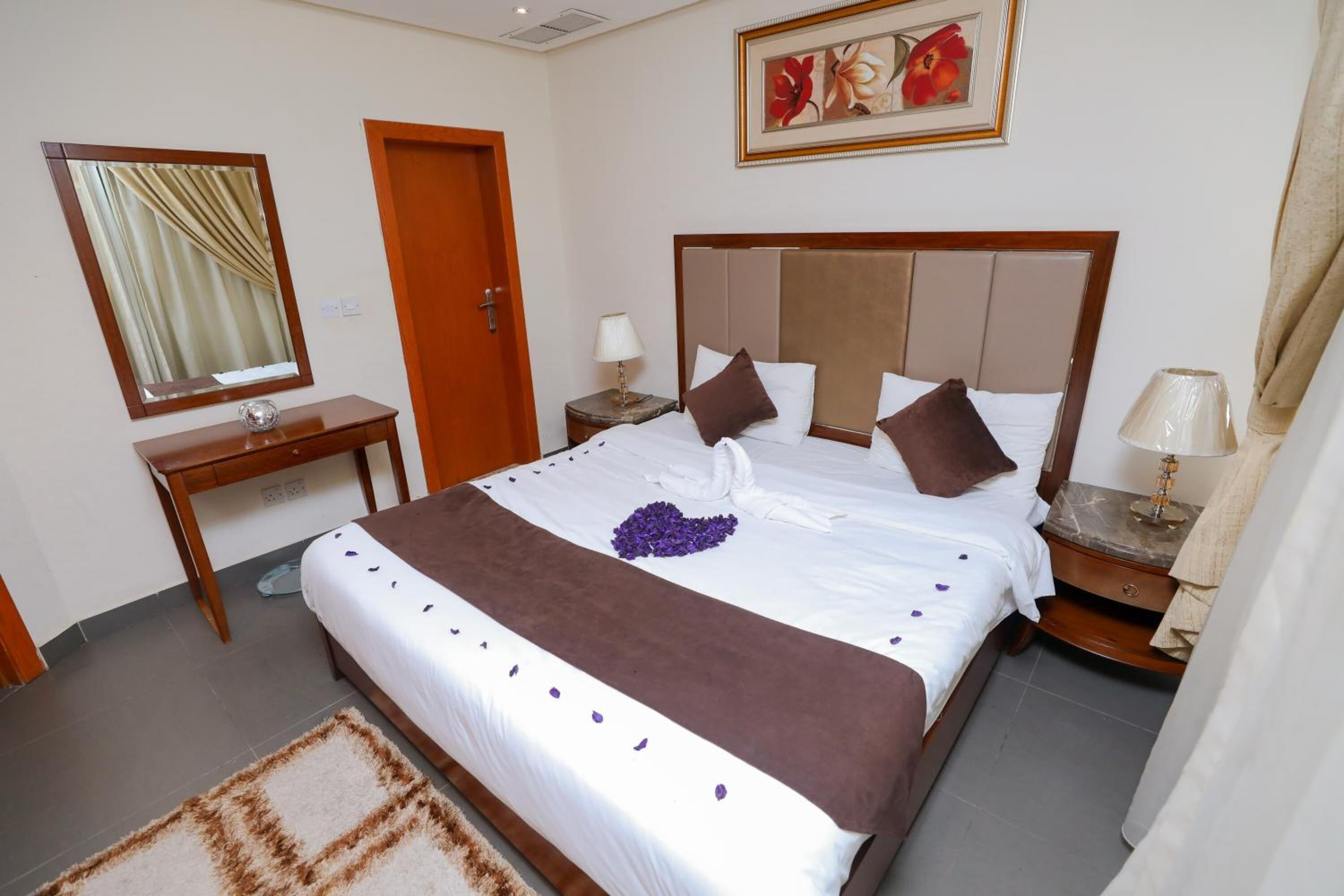 Habitación de hotel con una cama grande, un escritorio de madera, un espejo, una mesita de noche y un cuadro en la pared.