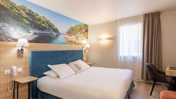 A hotel room with a bed, a desk, a chair, a phone, and a painting of a coastal landscape.