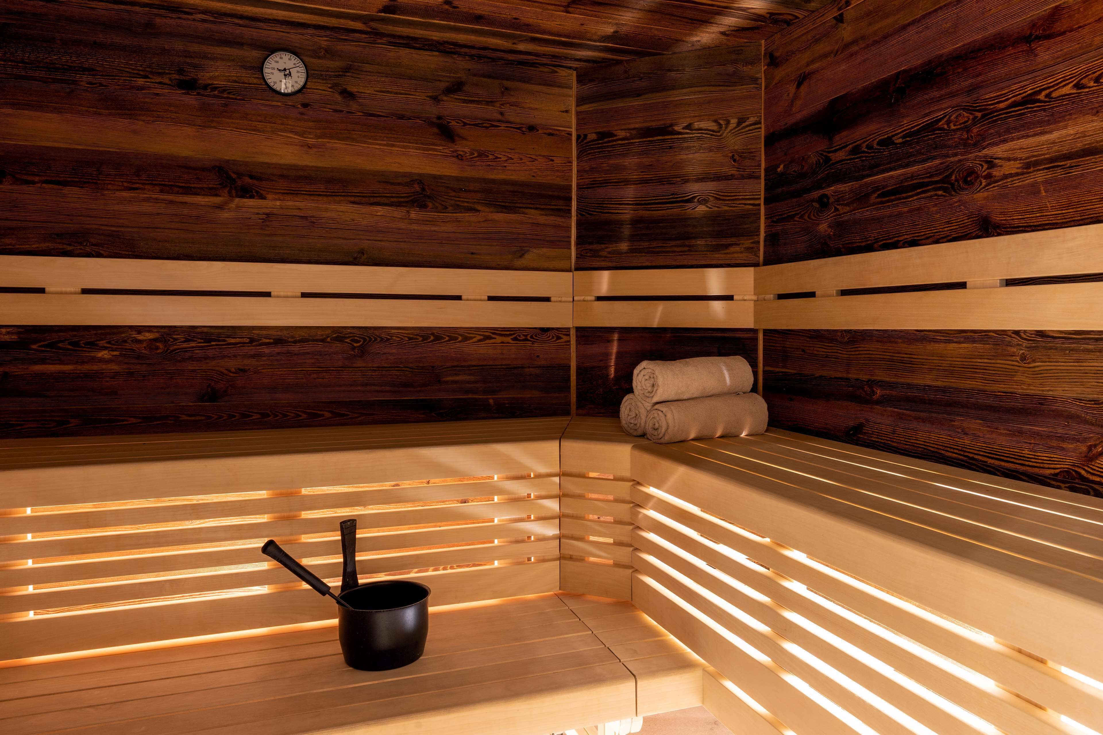 Un sauna con paredes de madera, un banco, un perchero para toallas y un cubo negro.